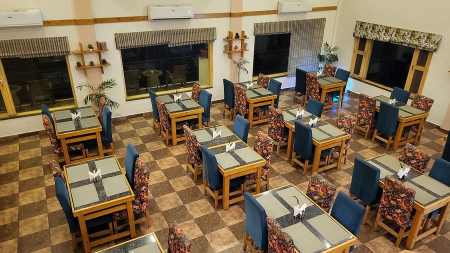 A spacious dining area with neatly arranged tables, wooden chairs, and a warm, inviting ambience at Dagshai Manor Kasauli - Inde Hotels