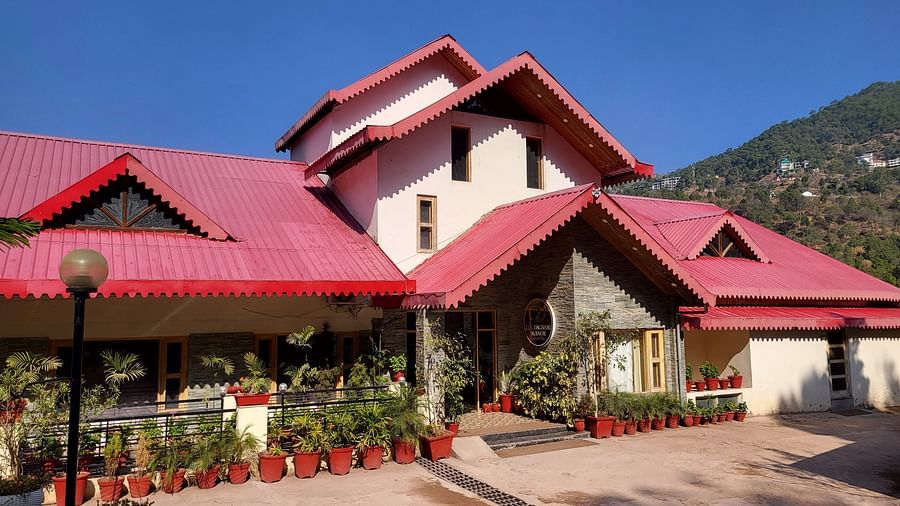 Facade with red rooftops, a landscaped entrance, and a clear blue sky in the background at Dagshai Manor Kasauli - Inde Hotels.