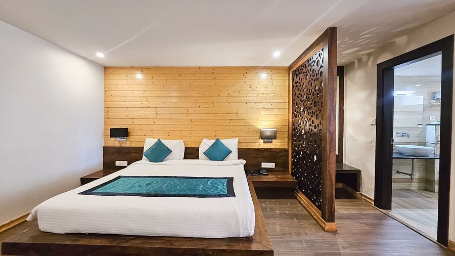 An image of an executive premium room featuring a bed, bed side tables, lamps, and a door leading to the washroom - Yashshree Sanderling, Darjeeling