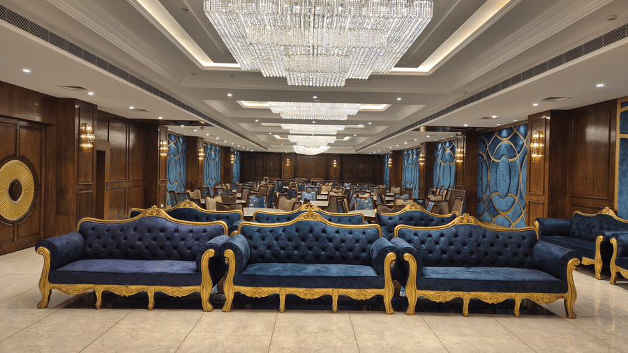 Banquet hall with blue and gold chairs, chandeliers, and large stage backdrop.