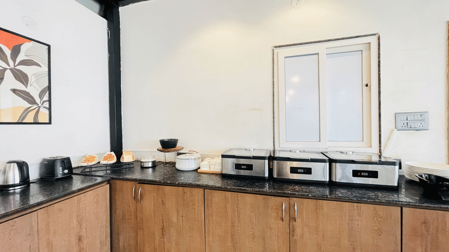  Buffet counter area at Hotel Kyzen Smart Stays Madhapur with wooden cabinets, dark granite top, multiple food warmers, and large windows with natural light.