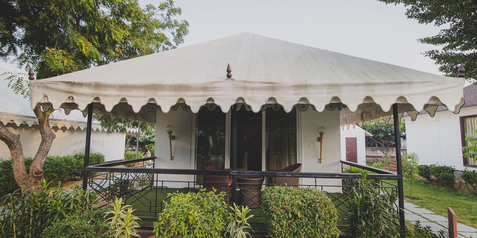 Facade of Royal Luxury Tent with Balcony surrounded by plants and trees at Rajasthali Resort & Spa Jaipur. 