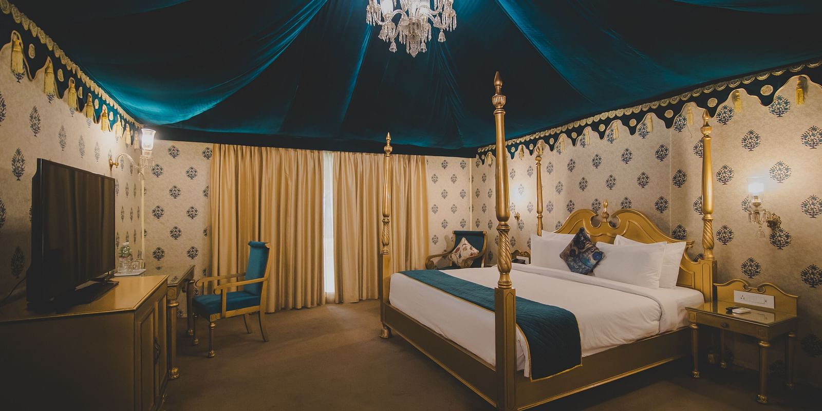 Image of Royal Luxury Tent with Balcony with a bed and a chandelier hanging from the ceiling at Rajasthali Resort and Spa.