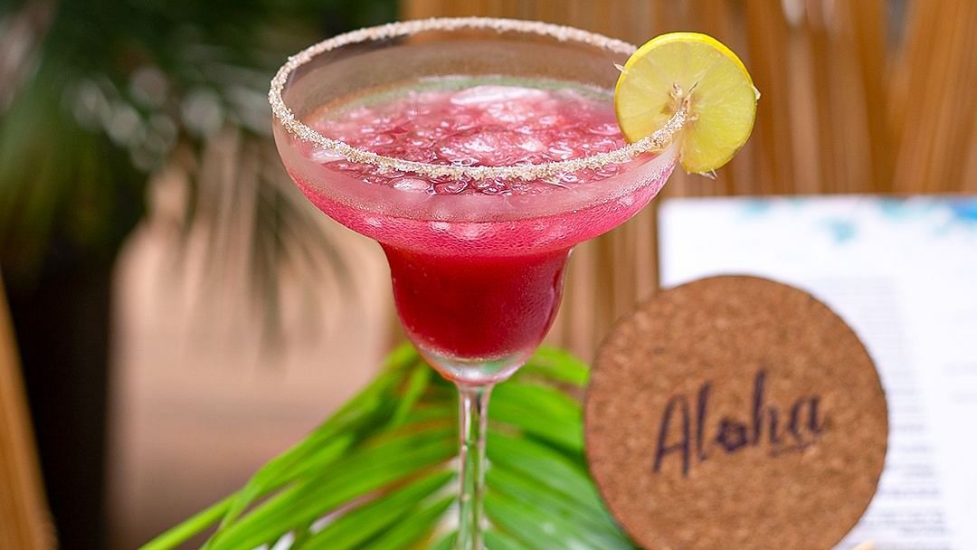 Pink margarita with lime and an Aloha coaster on a leafy table setting at Hotel Mumbai House Mindspace, Malad.