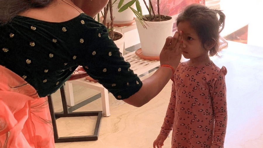 A person applies a mark on a child's forehead indoors at Amantra Shilpi Resort, Udaipur.