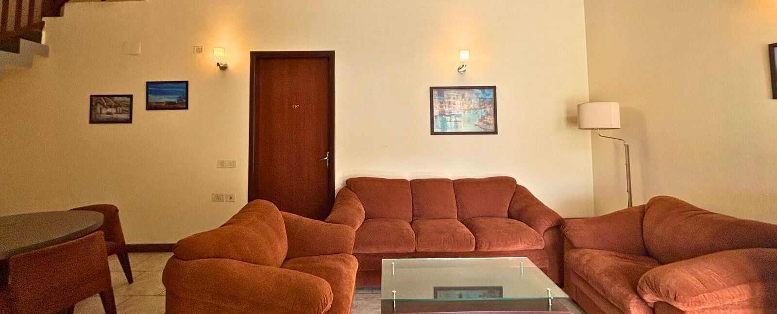 Living room with cosy seating and a high ceiling in the villa at Vedic Village Spa Resort, featuring brown plush couches.
