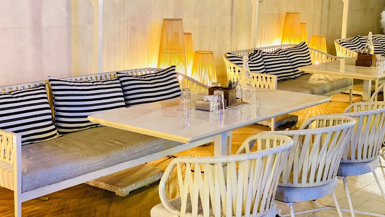Indoor dining area with white chairs, wooden tables, and striped cushions at Hotel Mumbai House Mindspace, Malad.