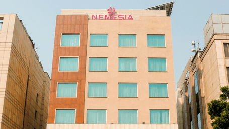 Facade of the Nemesia City Center in Gurugram featuring the hotel's entrance and its surrounding greenery.