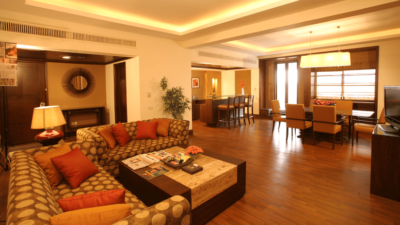 A hotel suite with sofas, tables, chairs, and warm lighting in the living area.