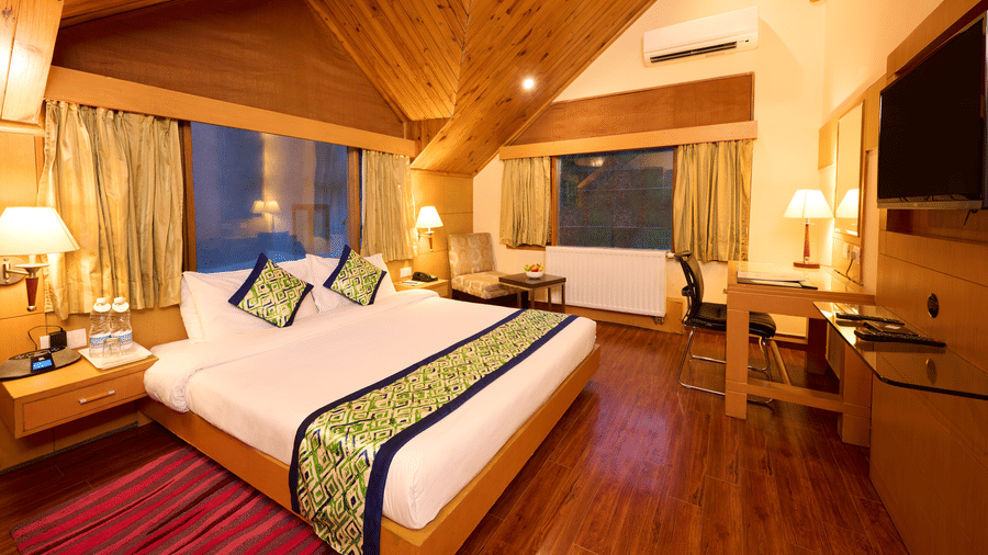 Renest Manali - interior view of the Hornbill bedroom featuring a king size bed with green throw pillows and bed scarf