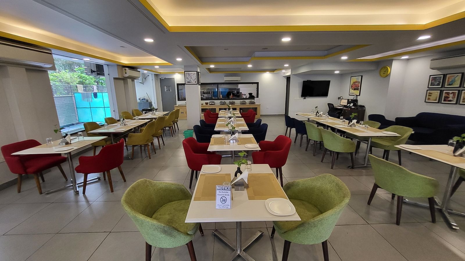 An image of a restaurant at Inde Hotel Golf Course Extension featuring several sets of chairs and tables where plates and table mats are placed