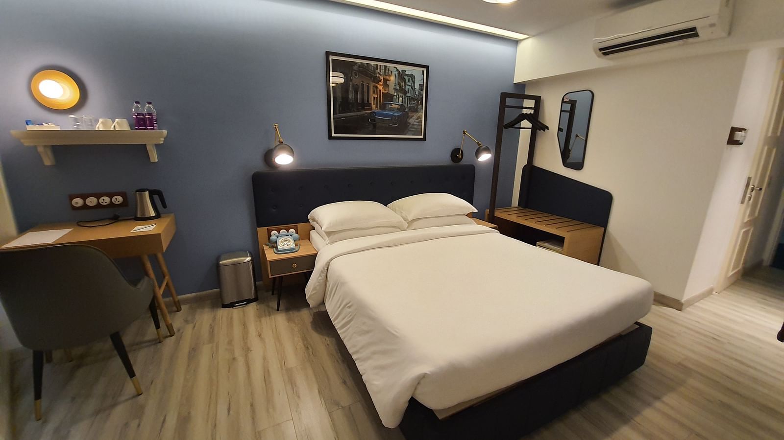 A spacious hotel room with a king size bed, a wooden desk with a chair, and a large window with a view. The room is decorated in a modern style with blue and white accents.  | T24 Retro