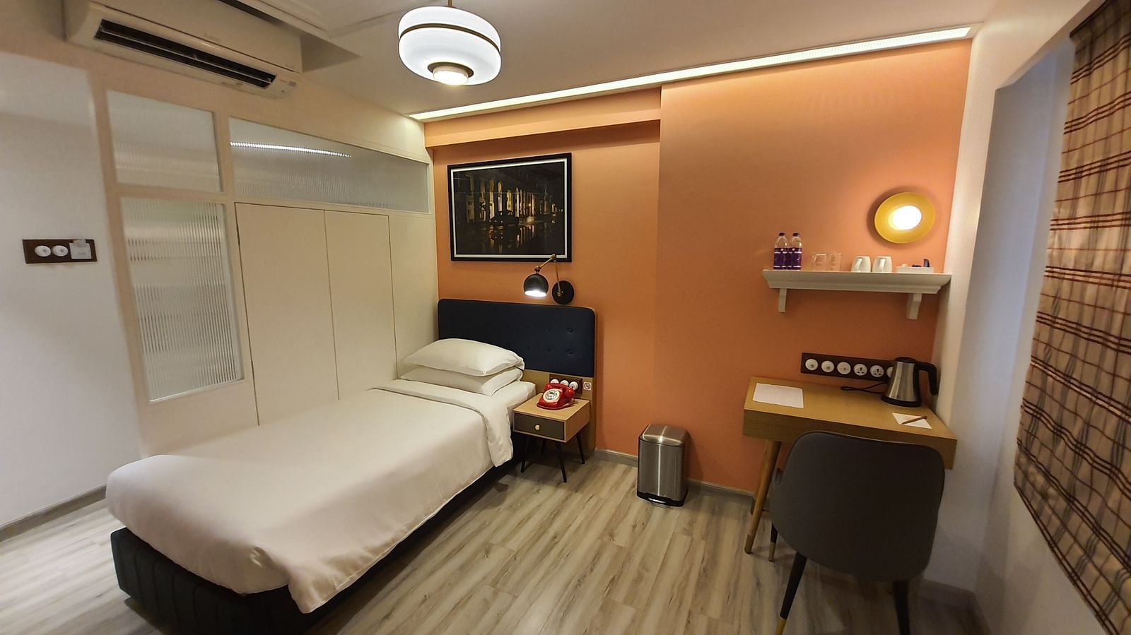 A cosy and well-lit hotel room with a single bed, a bedside table, a wardrobe, a work desk, and a window with curtains   | T24 Retro