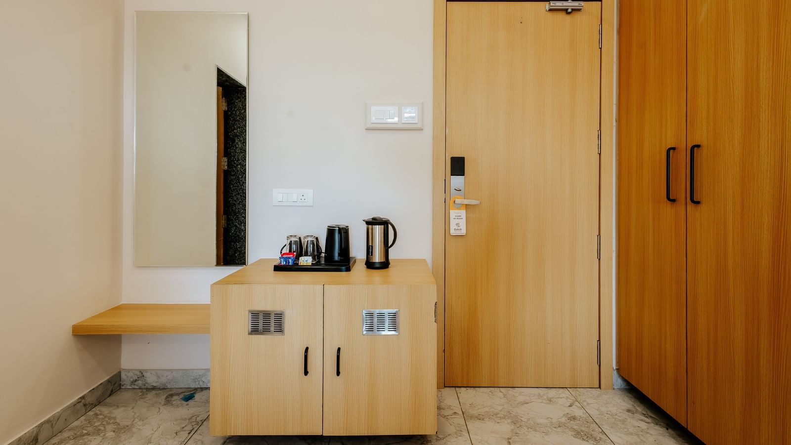A well-equipped room entry area at Daksh The Grand Gowardhan, Dwarka, with a wardrobe, a dressing table with a long rectangular mirror, and a refreshment station beside it.