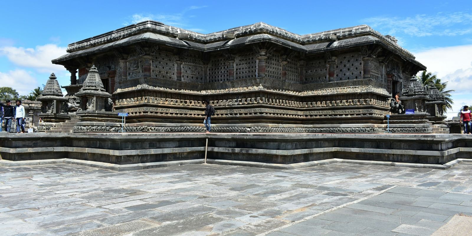 Facade of Chennakesava Temple in Belur with a stone courtyard in front of the temple and under a blue sky on a sunny day