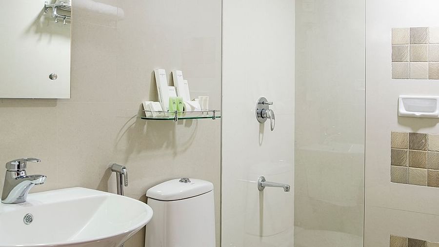 Bathroom with a glass-enclosed shower, white toilet, and dual sinks - Abad Copper Castle, Munnar