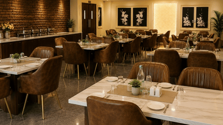 An indoor dining area or restaurant space with several set dining tables and brown chairs arranged under warm ceiling spotlights.