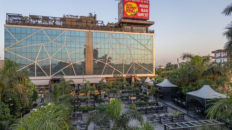 Front-facing view of Hotel Highway King, Jaipur's glass building with trees and outdoor seating visible below.