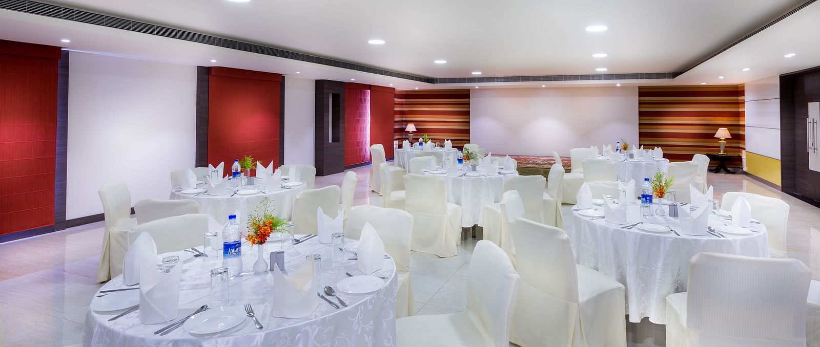 Interiors of a event hall with white chairs and tables at Regency Tiruttani by GRT Hotels.
