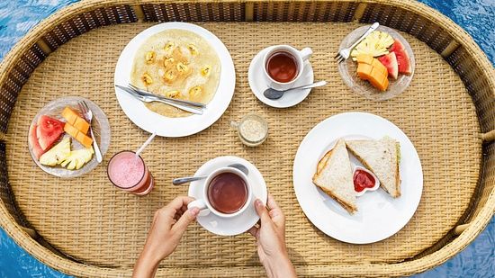 A wooden basket placed on the edge of a swimming pool, with breakfast served on plates