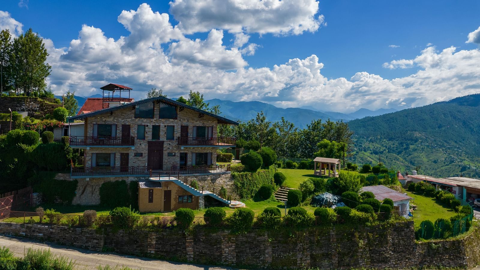 A charming villa surrounded by lush greenery and set against the backdrop of rolling hills and blue skies. - Blusalzz Homes The Himalayan Bungalow, Almora