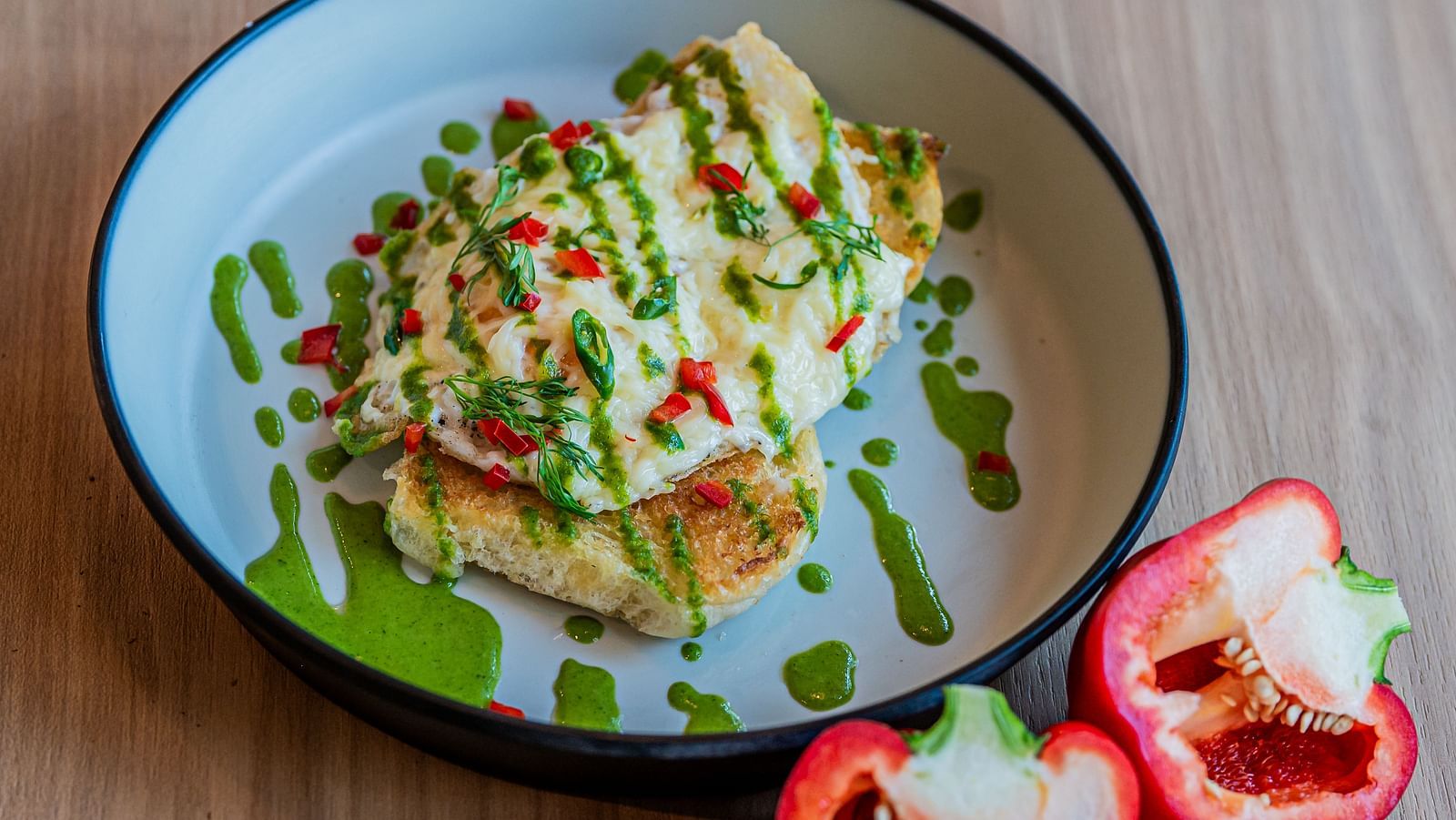 A plate of egg toast topped with sauces and veggies, with capsicum cut into two pieces and placed beside the plate, along with a chilli at Indie Stays Mumbai International Airport.
