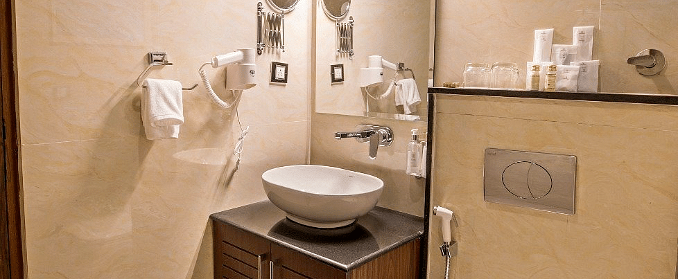 A brightly lit bathroom at Regenta Inn DLS featuring a vanity area along with a commode besides it.