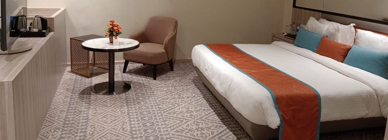 Modern hotel room with twin beds, a small table and chair, soft lighting, and minimalist decor.