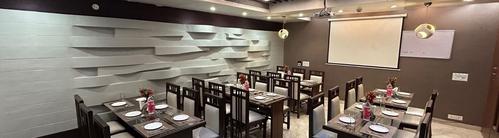A spacious restaurant with multiple dining tables, a minimalist grey design, and a whiteboard in the background - Hotel Emerald, Chandigarh