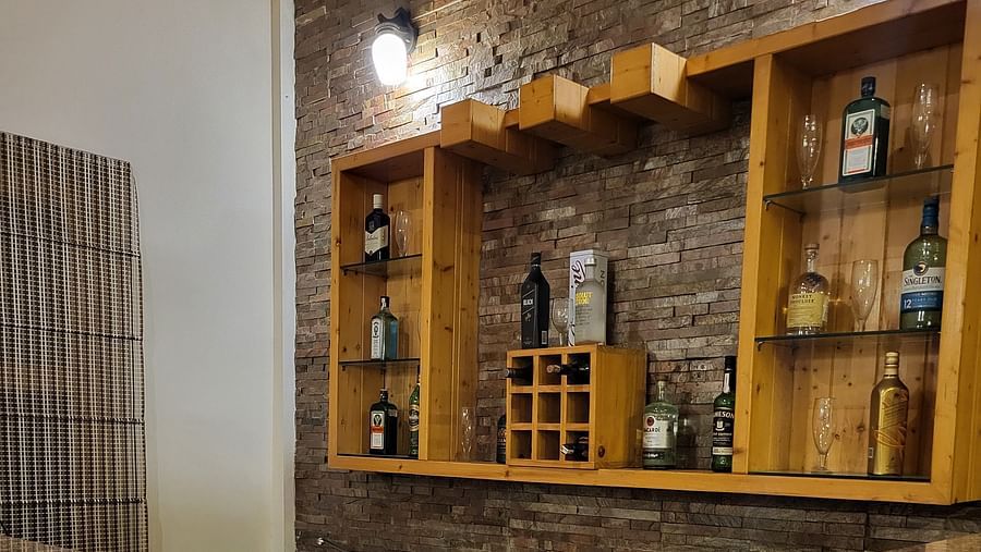A stylish bar area with a polished granite countertop, wooden shelves, and an elegant display of bottles at Dagshai Manor Kasauli - Inde Hotels.