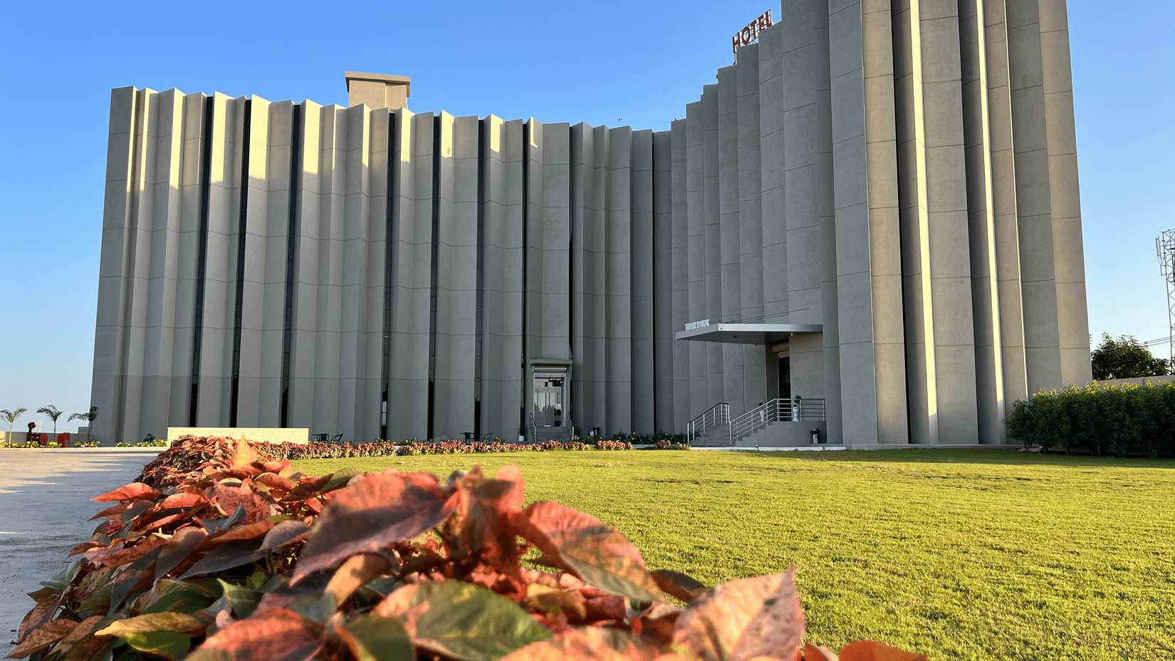 A facade view of VITS Jamnagar, Mithoi, with the party plot in Jamnagar featuring a manicured lawn and the multi-storied hotel behind it.