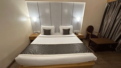 An overview of the Deluxe Rooms in Silvassa with a double bed, side table, headboard mounted lamps and a seating area at VITS Kamats Resort, Silvassa.