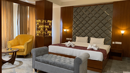A bedroom at Hotel Hyderabad Grand, Shamshabad featuring a king size bed, a sofa, a sofa chair, centre table, bedside table with lights, and more.