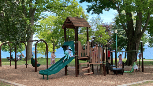 A view of a children's park with a slide as well as swings in view and a lake in the distance, highlighting Pookode Lake Activities.