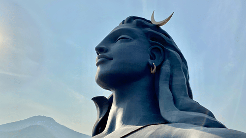An overview of the statue of Adiyogi Shiva with a mountain in the background, as seen during day time. It is one of the best places to visit near Coimbatore.