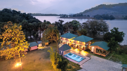 The illuminated facade of Ibex Resorts, Malampuzha (Kava Eco Camp and Caravan Park), featuring trees, and greenery at night.