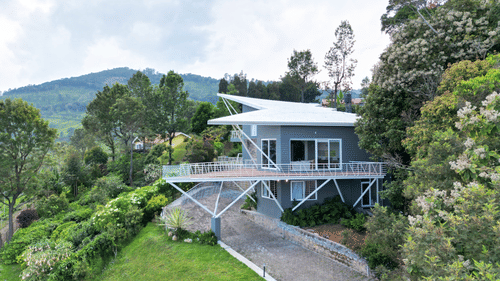 An aerial view of a modern grey resort villa with a white roof and a spacious balcony, nestled amidst lush greenery and hills - Ibex Resorts, Coonoor (Tapas)