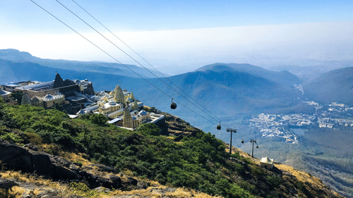 A jain temple in view on top of mount girnar with mountains in the distance in view as well