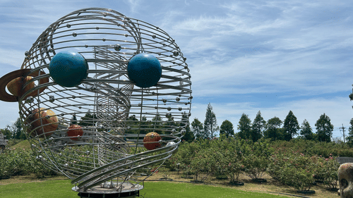 Science-inspired metal sculpture displayed in a landscaped garden.