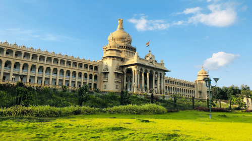 Vidhana Soudha in Bangalore with a lawn are in the foreground, small shrubs near the building and blue sky in the background