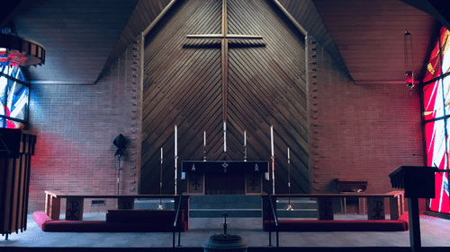 A big cross on the altar with painted glass windows on the side