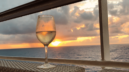 A glass of liquor kept on a table on a boat with the sunset in the backkground