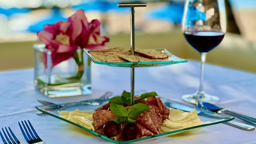  A layered dish on a white table setting with wine and flowers, with ocean views in the background served at The Soco Hotel.