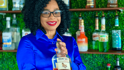 A female bartender in a blue shirt showcasing a drink behind the bar at The Soco Hotel.