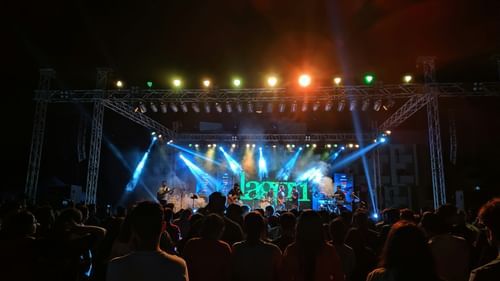 Stage performance with musicians under green and blue stage lights, viewed from the crowd.