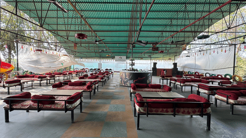 An overview of the open-air setting at Urban Dhaba in Silvassa with dhaba styled seating, cushions on the seats, a reception desk in the centre, and trees outside VITS Kamats Resort, Silvassa.