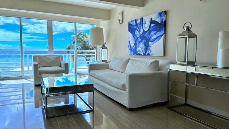 A stylish beachfront living room at The Soco Hotel, featuring modern furnishings, wall art, expansive windows, and a stunning ocean view.