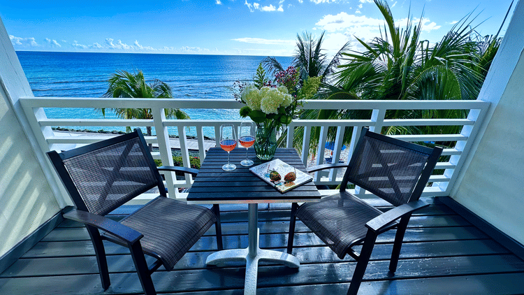 Outdoor dining setup with ocean view and palm trees at The Soco Hotel, featuring two black chairs and a small table.