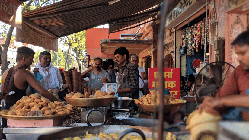 A small local roadside store selling fresh kachoris and samosas to the customers lining in front of them.