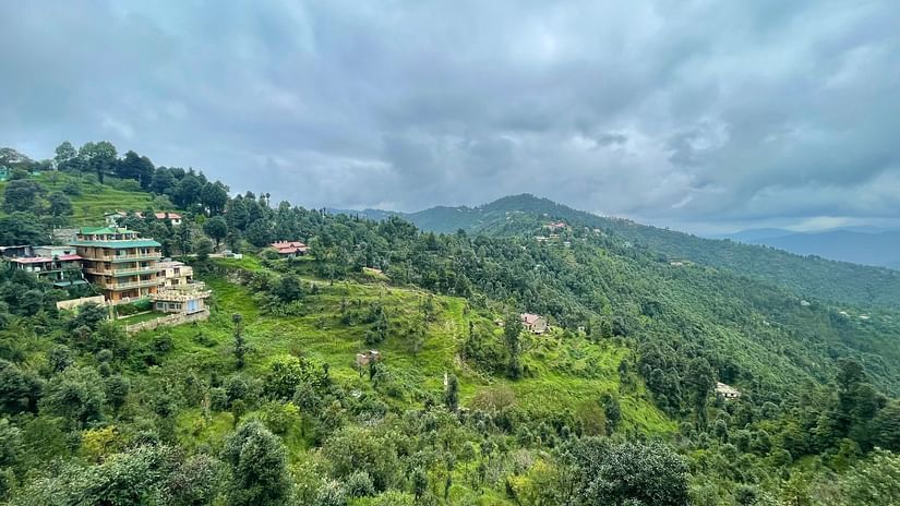 Rolling green hills covered in dense vegetation and scattered structures stretch out under a cloudy sky, depicting a serene rural or mountainous landscape